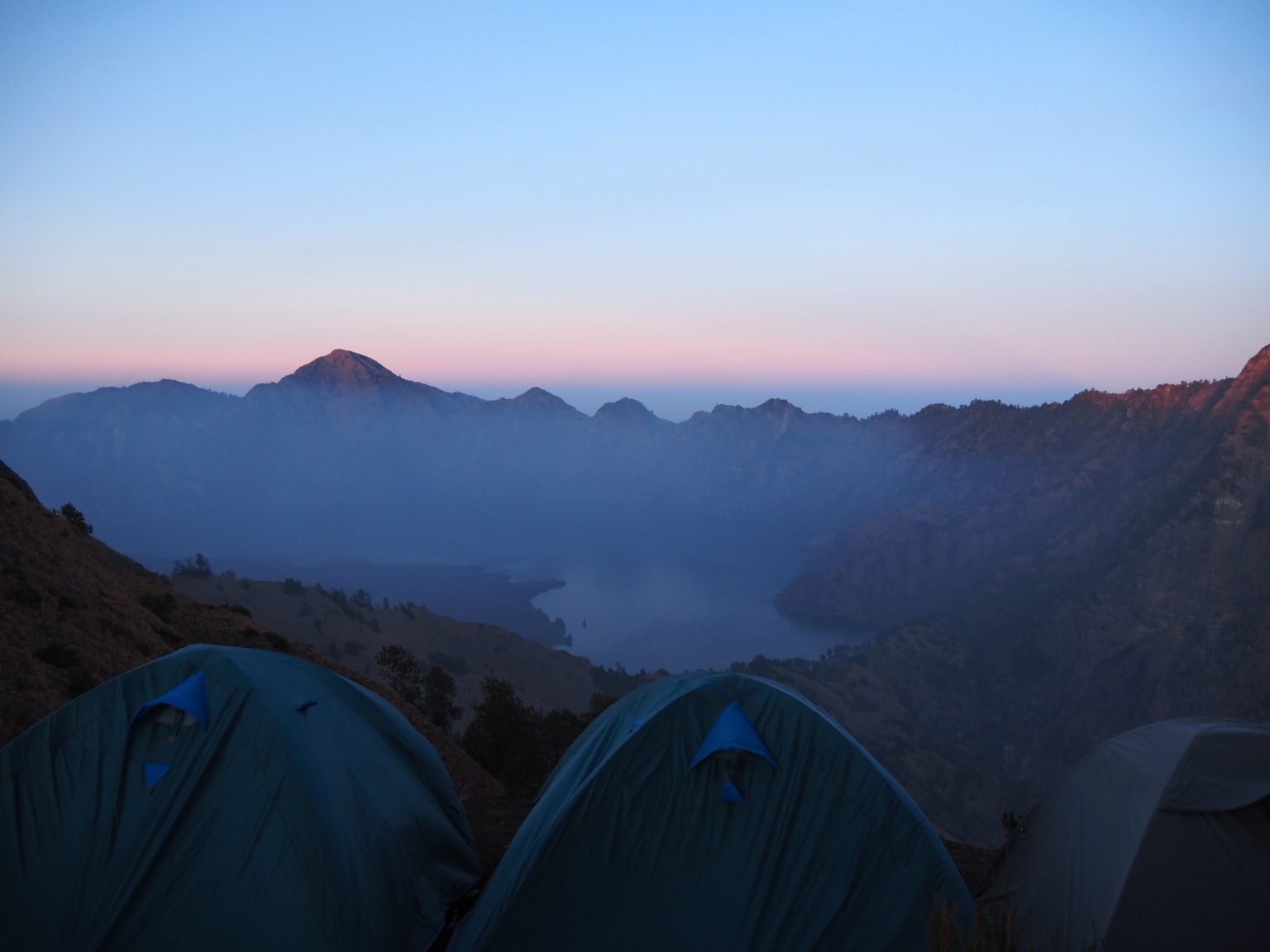 Tents on the crater rim of Mount Rinjani, with the crater lake and mountains at dawn