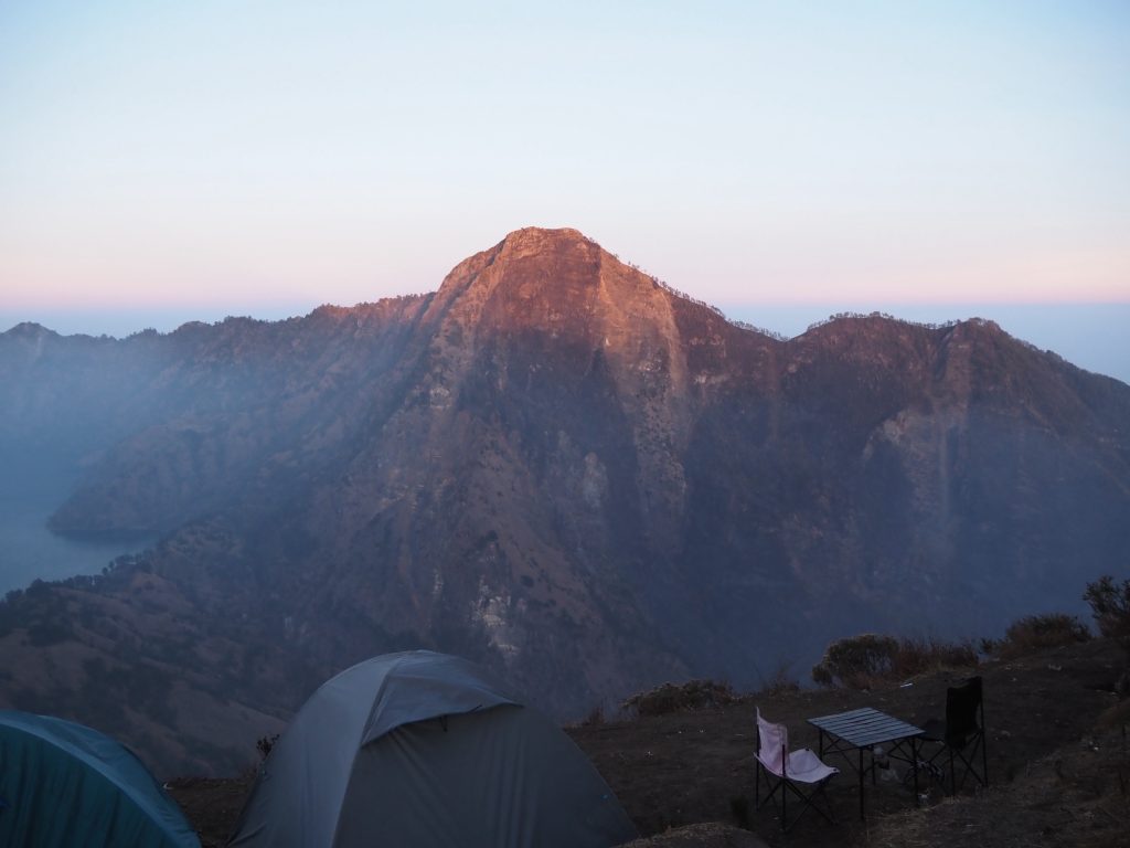 Crater rim peak lit by sunrise above the crater lake, with tents at the campsite